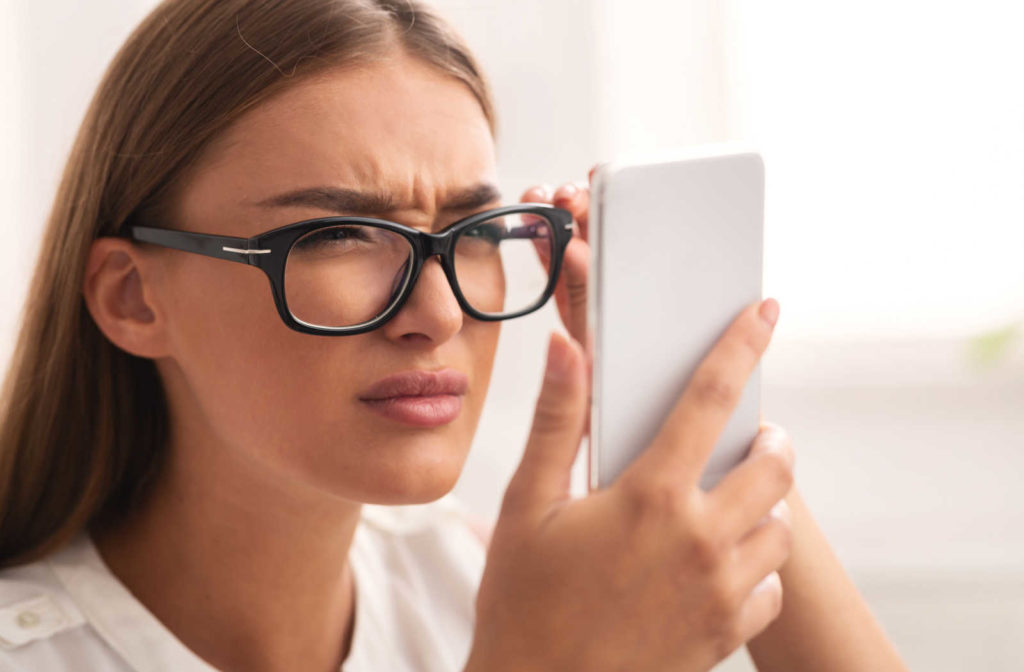 A girl with myopia is squinting while holding her phone close to her face and looking at her cell phone screen.