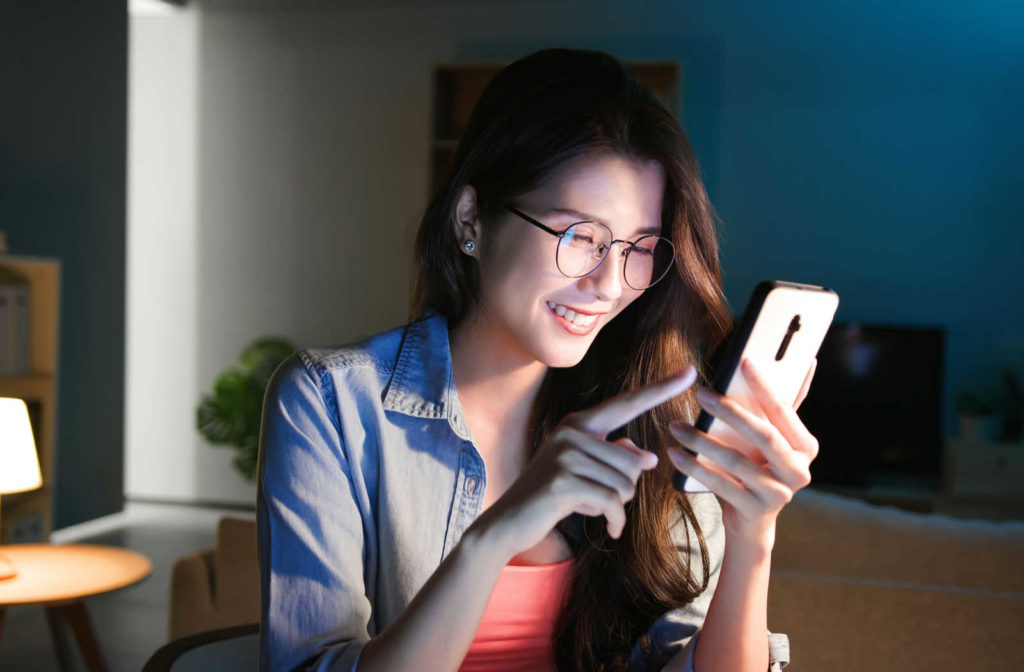 A young girl wearing eyeglasses while using her smartphone at home at night.