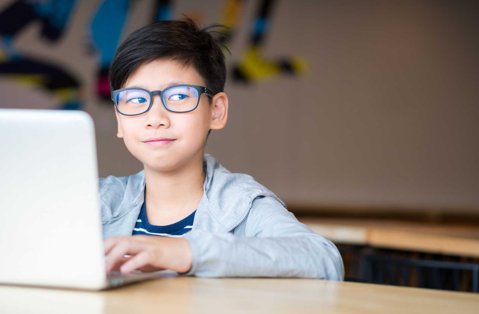 A young boy sis wearing blue light glasses during his online classes while studying in front of his computer at home.