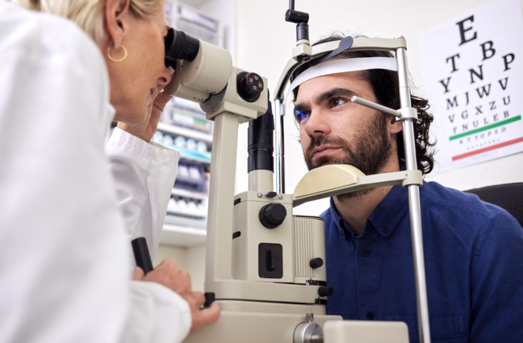 A female optometrist examining the eyes of a man using a medical device to detect potential eye problems.